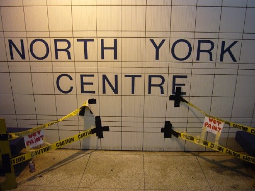 Letters in Helvetica on tile wall read NORTH YORK CENTRE. Wet Paint caution tape is duct-taped to the wall