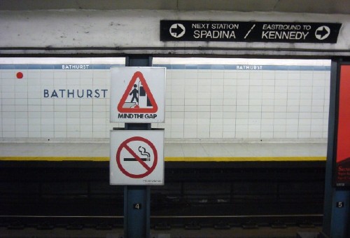 Sign over platform divider has arrows in a circle and reads NEXT STATION SPADINA / EASTBOUND TO KENNEDY in Helvetica
