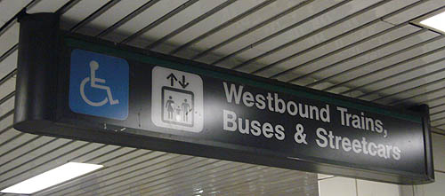Sign has wheelchair and elevator pictos and reads Westbound Trains, Buses & Streetcars