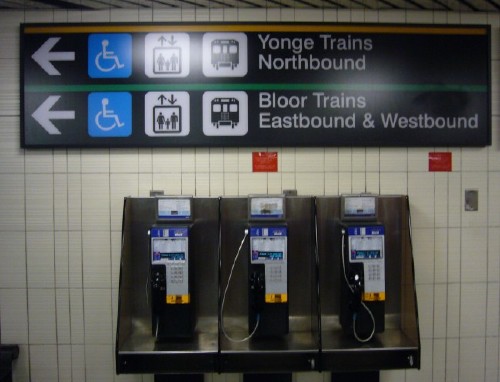 Sign has yellow line across top and green line across middle, with identical arrows and pictographs and legends Yonge Trains Northbound and Bloor Trains Eastbound & Westbound