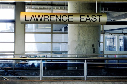 Curved metal sign hanging in front of windows reads LAWRENCE EAST