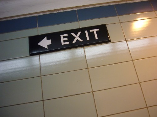 Viewed at an angle, sign affixed to green tile wall reads EXIT