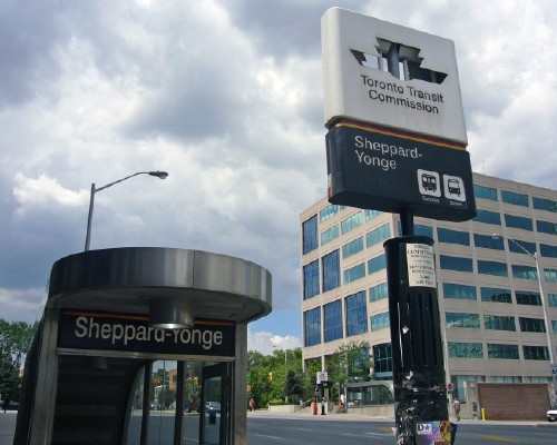 Sign over entrance reads Sheppard-Yonge. Nearby pylon sign is missing its TTC logo, with sky visible straight through the hole