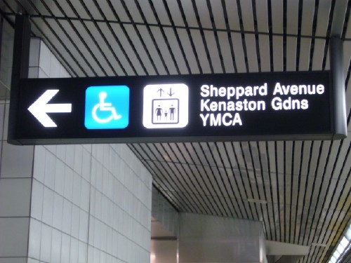 Sign with arrow and two pictos reads Sheppard Avenue Kenaston Gdns YMCA