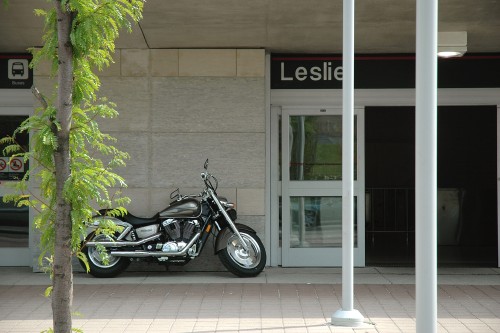 Exterior sign, in badly-letterspaced ‘Helvetica,’ reads Leslie. A motorcycle is parked against the wall