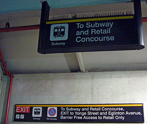 One hanging and one wall-mounted sign both say To Subway and Retail Concourse, among other things