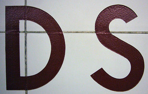 Letters DS in brown paint on a tile wall