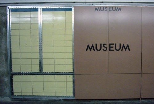 Brown panels on wall read MUSEUM alongside metal frames sitting on top of original cream-coloured tile wall