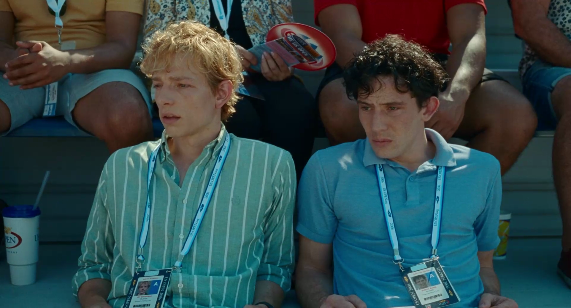 Honey-blond‑ and jet-black-haired tennis players seated in stands