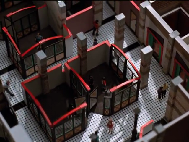 Overhead view of diorama shows mezzotint-patterned flooring, office cubicles with red-topped walls