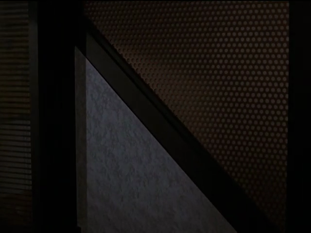 Wall diagonally divided between mottled grey panelling and bronze mesh