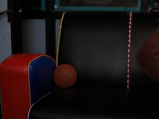 Upholstered chair with thick, high-contrast piping and red arm with blue inner wall, on which sits a dark red ball