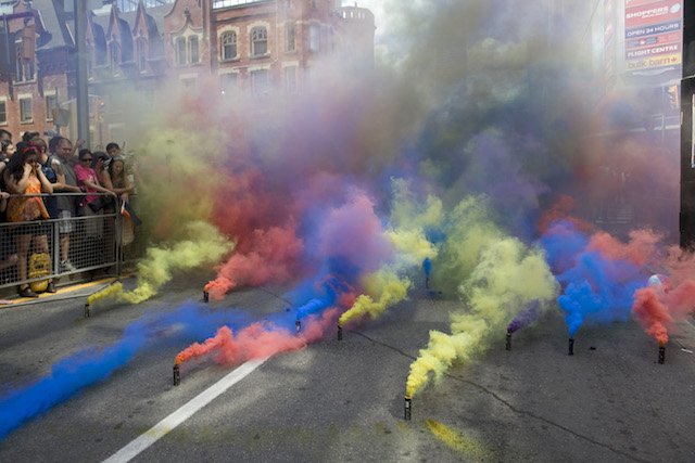 Ten or so smoke grenades, standing a few inches upright on the street, emit green, orange, or blue smoke