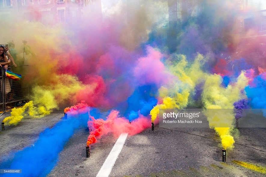 Closeup of multicoloured smoke obscuring most of the view above a street (some standing canisters visible)