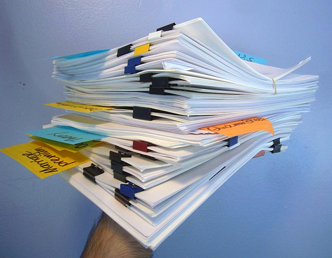 Hand holding eight-inch stack of papers with coloured alligator clips and Post-Its