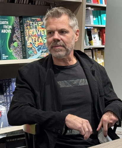 Russell Smith (full head of hair; crossed fingers) in black T‑shirt and sweater